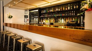 A bar area with a wooden counter, multiple stools, and shelves stocked with various liquor bottles. - Bay Plaza Hotel (Wellington)