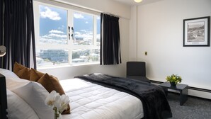 A hotel room with a large bed, a view of the city, a small table with a plant, and a framed picture on the wall. - Bay Plaza Hotel (Wellington)