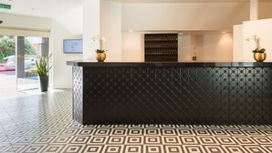A reception area with a black counter, patterned floor tiles, and two potted plants. - Bay Plaza Hotel (Wellington)