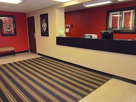 Zona de recepción de un hotel con pared roja, un mostrador de recepción, un banco y una alfombra a rayas.