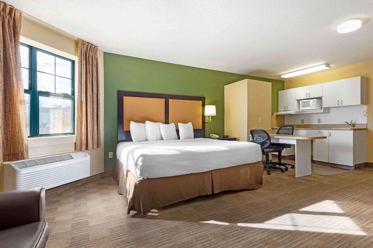 A hotel room with a bed, desk, and kitchenette.