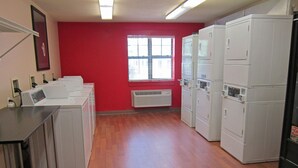 A laundry room with multiple washing machines, a window with blinds, and a red wall.