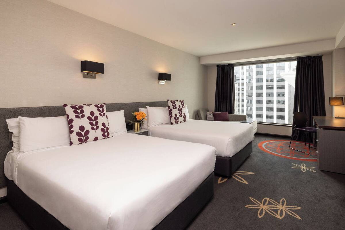 A hotel room with two beds, a desk, a chair, and a large window with curtains.