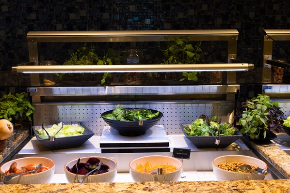 Un buffet proposant une variété de plats, notamment des salades, des légumes et des légumineuses.
