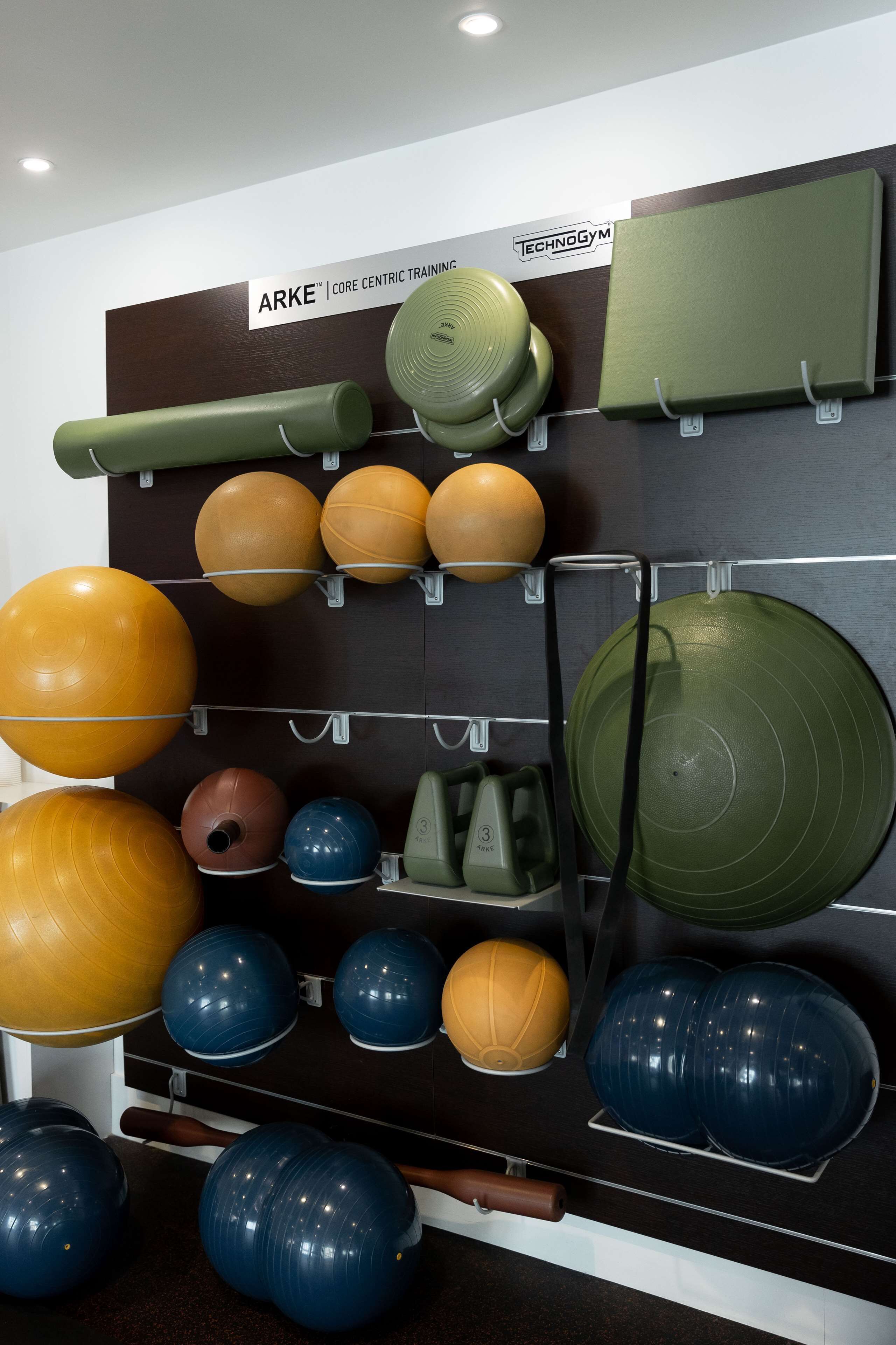 Un présentoir mural où sont exposés des ballons d’exercice de différentes tailles et couleurs, avec une pancarte au-dessus indiquant : « ARKE | ENTRAÎNEMENT CIBLE SUR LES MUSCLES DU TRONC ».
