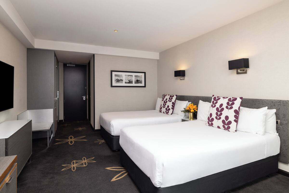 A hotel room with two beds, a desk, a TV, and a framed picture on the wall.