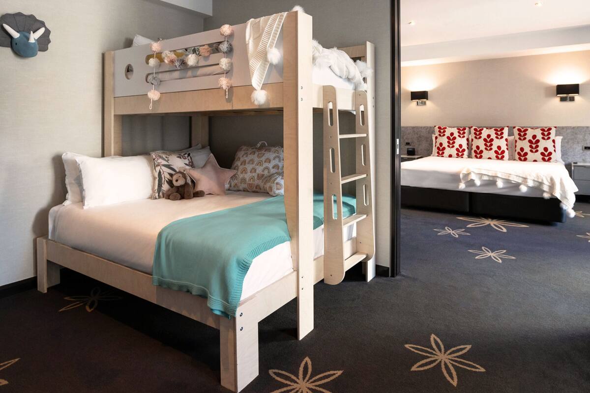 A bunk bed with a ladder, a separate bed with a red and white patterned headboard, and a carpet with a floral design.