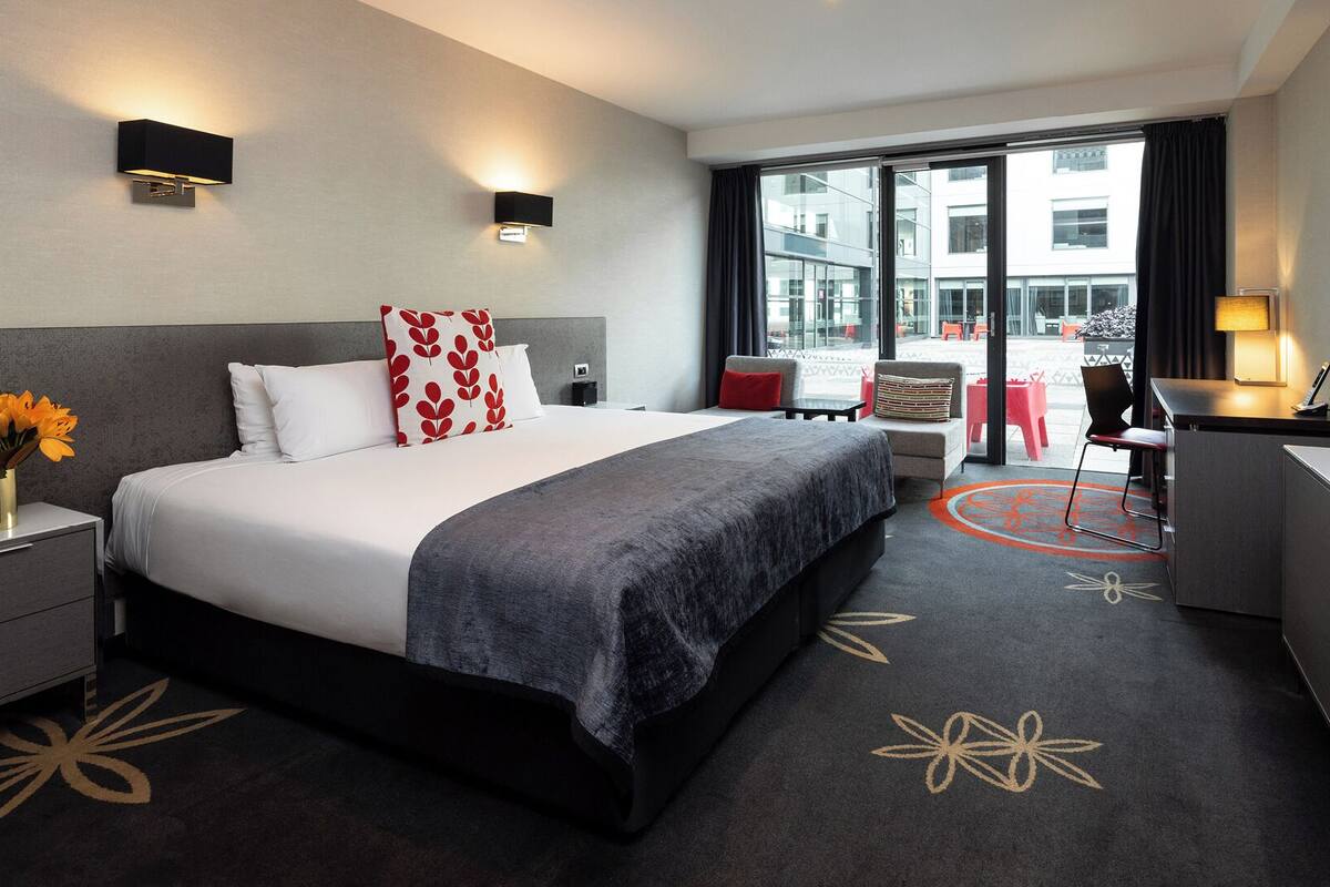 A modern hotel room with a large bed, bedside tables, a desk, and a TV.