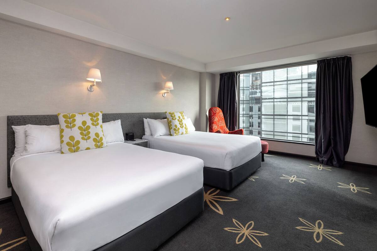 A hotel room with two beds, a large window with curtains, and a chair.
