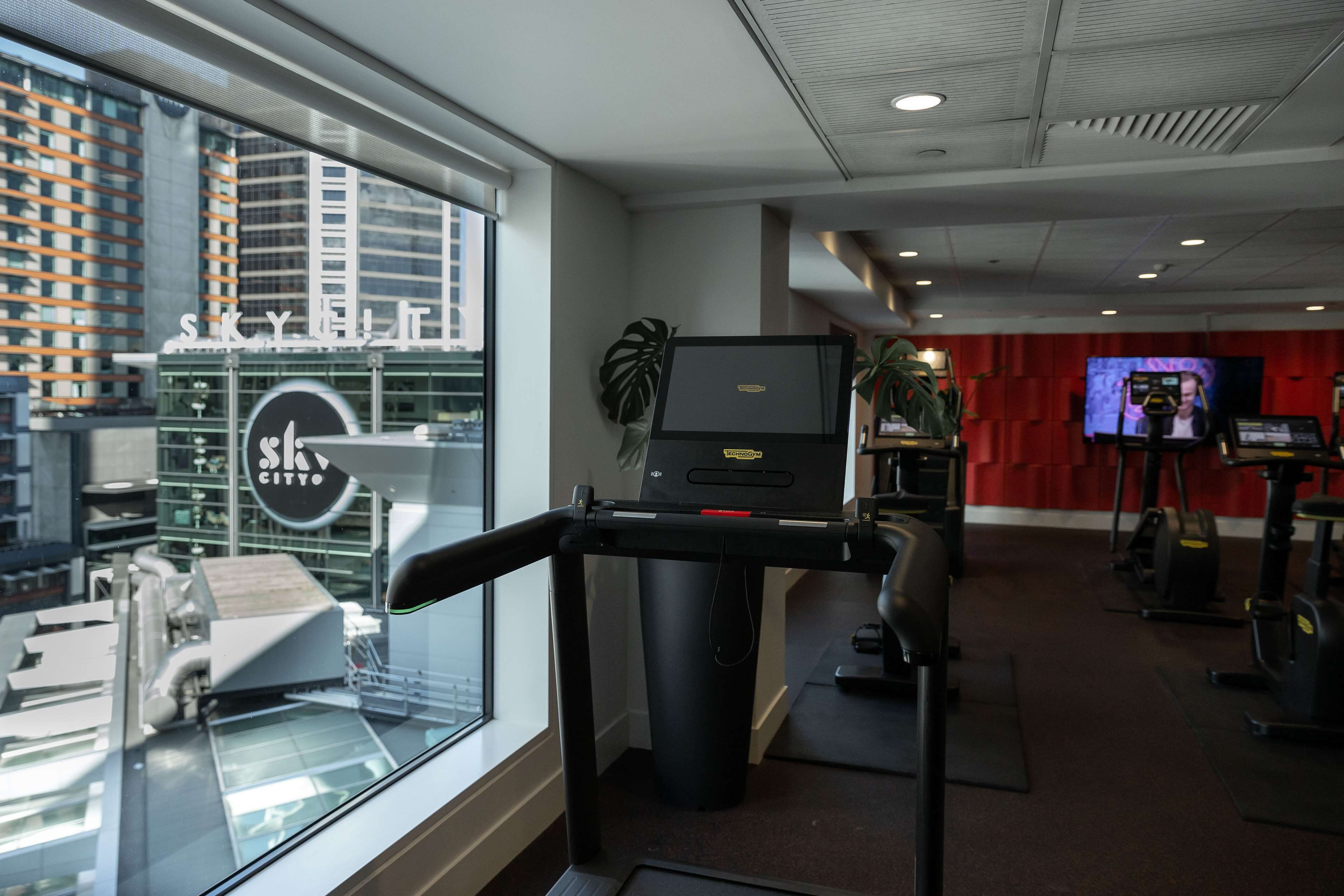 A gym with treadmills, stationary bikes, and a large TV screen.