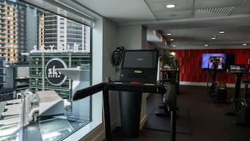 A gym with treadmills, stationary bikes, and a large TV screen.
