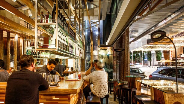 A bar area with wooden shelves and stools, a counter with a person serving, and a view of the street outside. - SkyCity Hotel (Auckland)