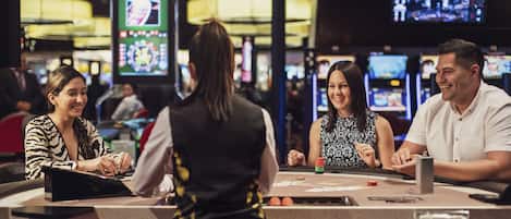A casino with multiple gaming tables and a large screen displaying a game.