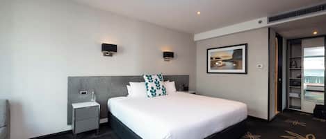 Une chambre d’hôtel avec un grand lit, une table de chevet, une lampe fixée au mur et un tableau encadré au-dessus du lit.