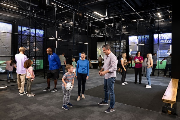 A modern indoor space with a high ceiling, visible structural beams, and large digital screens displaying content.