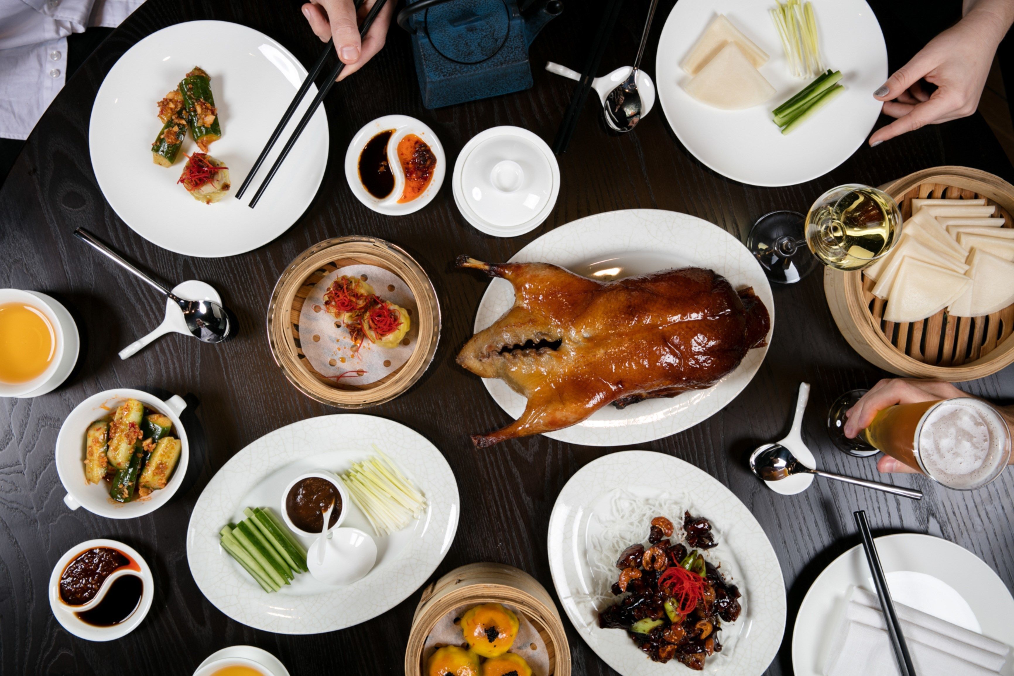 Een eettafel met verschillende gerechten, waaronder een hele gebraden eend, dumplings en groenten.