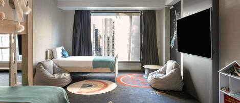 A hotel room with a bed, two bean bags, a small round table, a TV, and a bookshelf with books.