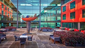 A modern outdoor seating area with tables and chairs, a central decorative sculpture, and a glass building facade in the background. - SkyCity Hotel (Auckland)
