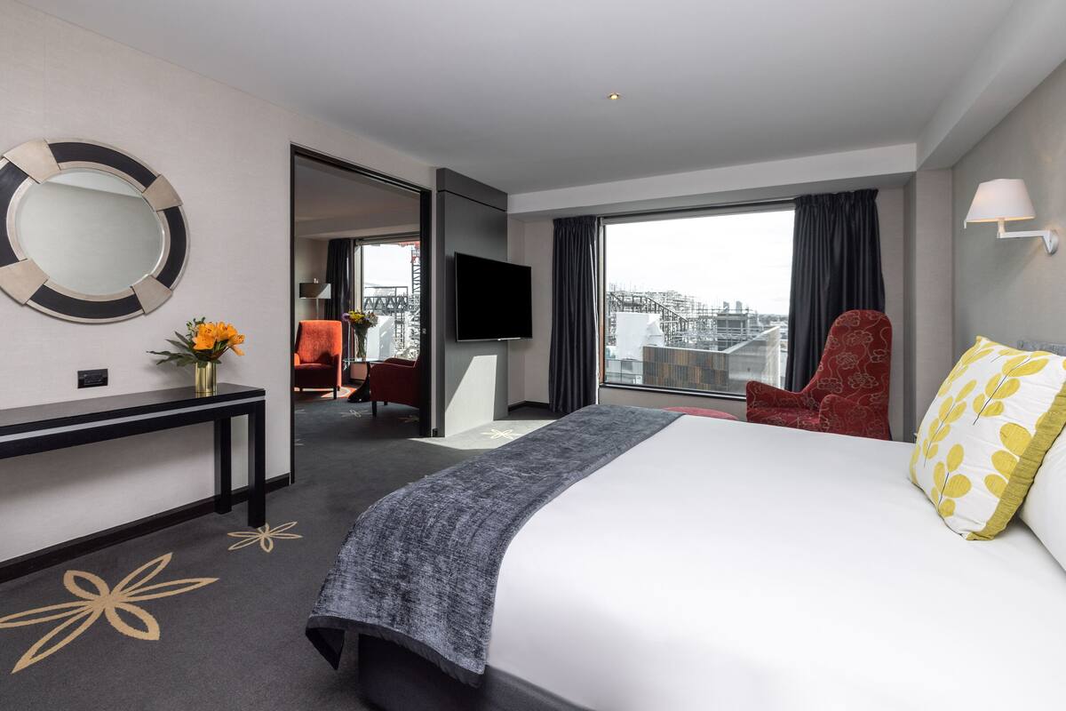 A hotel room with a bed, a desk, a chair, a TV, and a window with a city view.