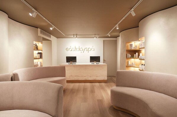 Un espace d’accueil de spa au design moderne, comprenant un comptoir d’accueil, deux téléviseurs et un plancher en bois clair.