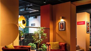 A cozy lounge area with a red sofa, a small table, and a potted plant. - Leonardo Hotel Amsterdam Leidse Square (Amsterdam)