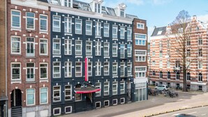 A multi-story building with a mix of brick and dark-colored facades, multiple windows, and a visible entrance with a red awning. - Leonardo Hotel Amsterdam Leidse Square (Amsterdam)