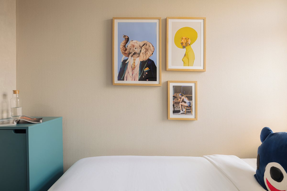 Una habitación de hotel con una cama, una mesita de noche con lámpara y tres cuadros en la pared.