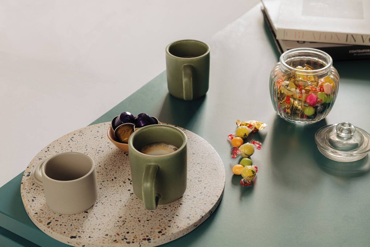 Dos tazas sobre un plato moteado, un tarro de caramelos variados y un libro en una mesa.