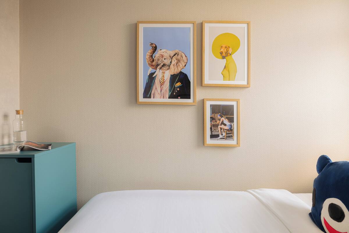 A hotel room with a bed, a nightstand with a lamp, and three framed artworks on the wall.