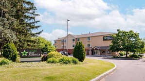 A Stay America hotel with a sign indicating extended stay options, surrounded by greenery and a parking lot. - Extended Stay America Suites Syracuse Dewitt (East Syracuse)