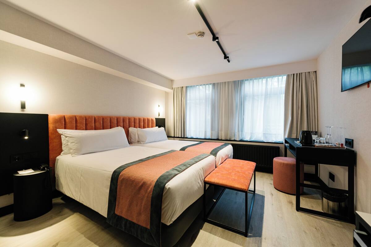 A modern hotel room with a large bed, a desk, and a window with curtains.