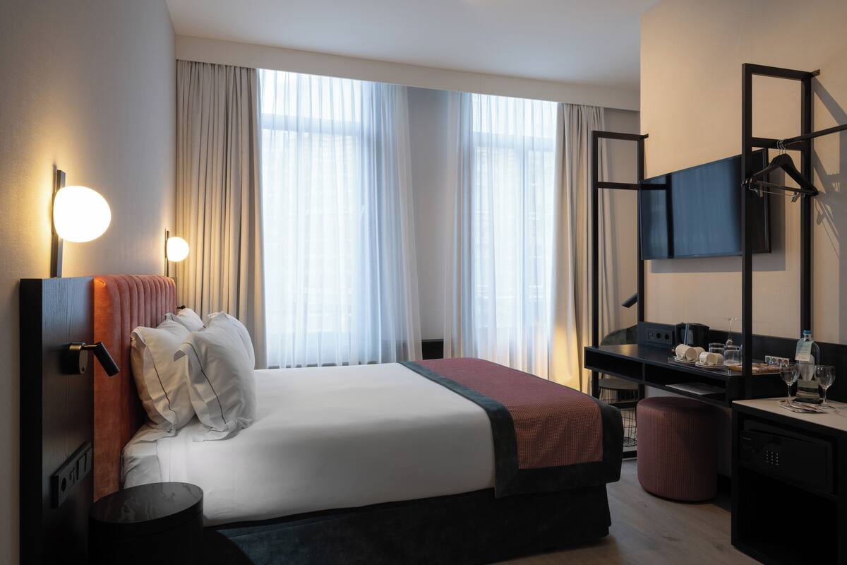 A modern hotel room with a large bed, a desk with a flat-screen TV, and a seating area.
