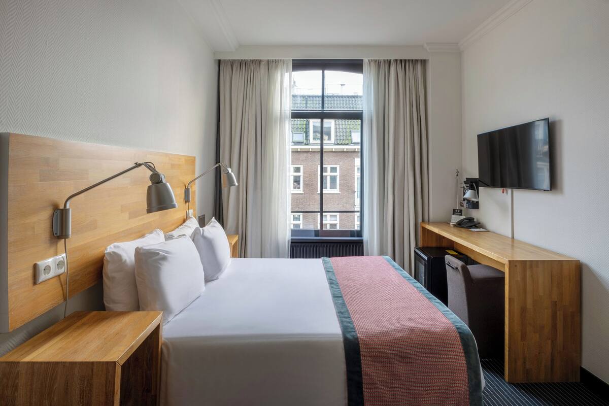 A hotel room with a bed, a desk, a TV, and a window with curtains.
