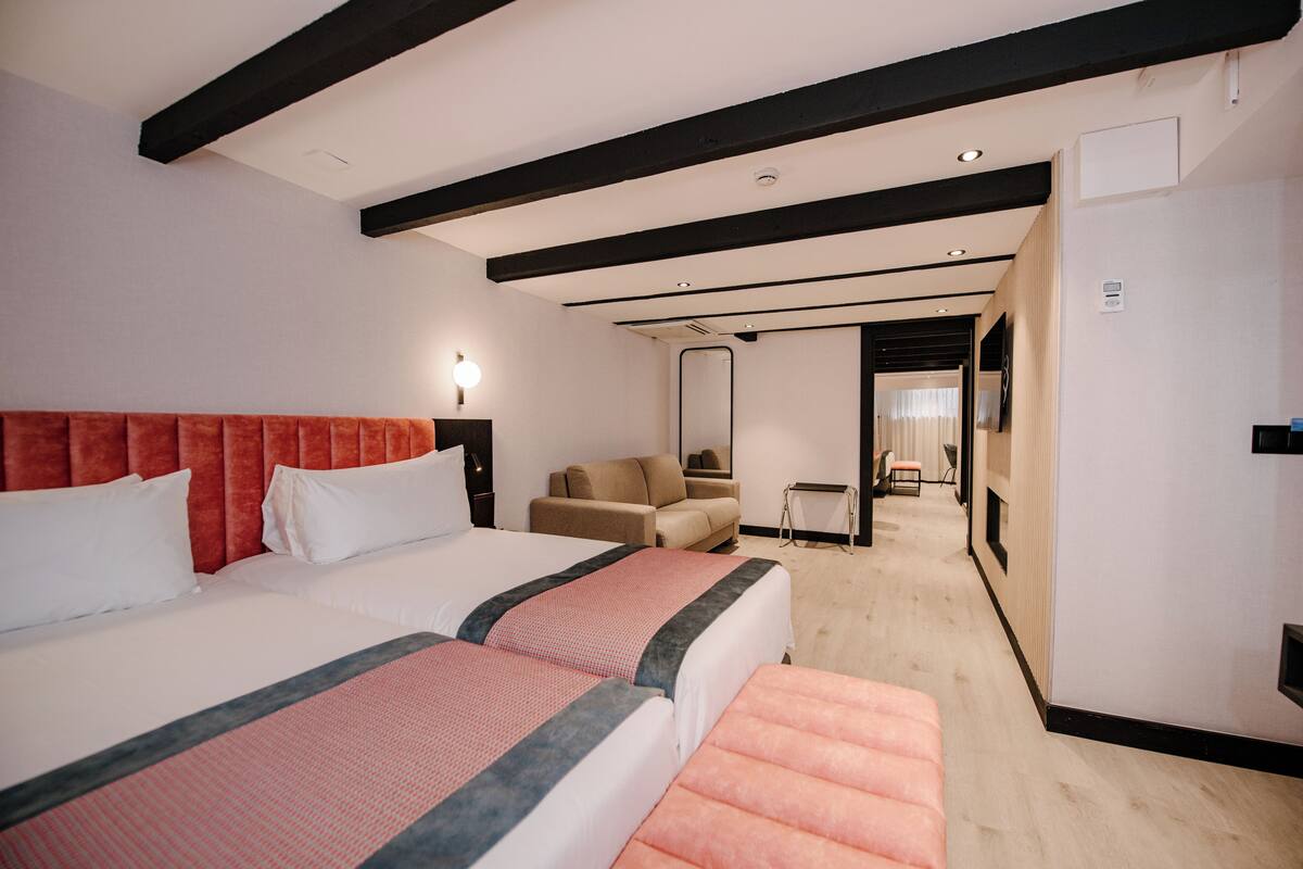 A hotel room with two beds, a sofa, a desk, and a mirror.