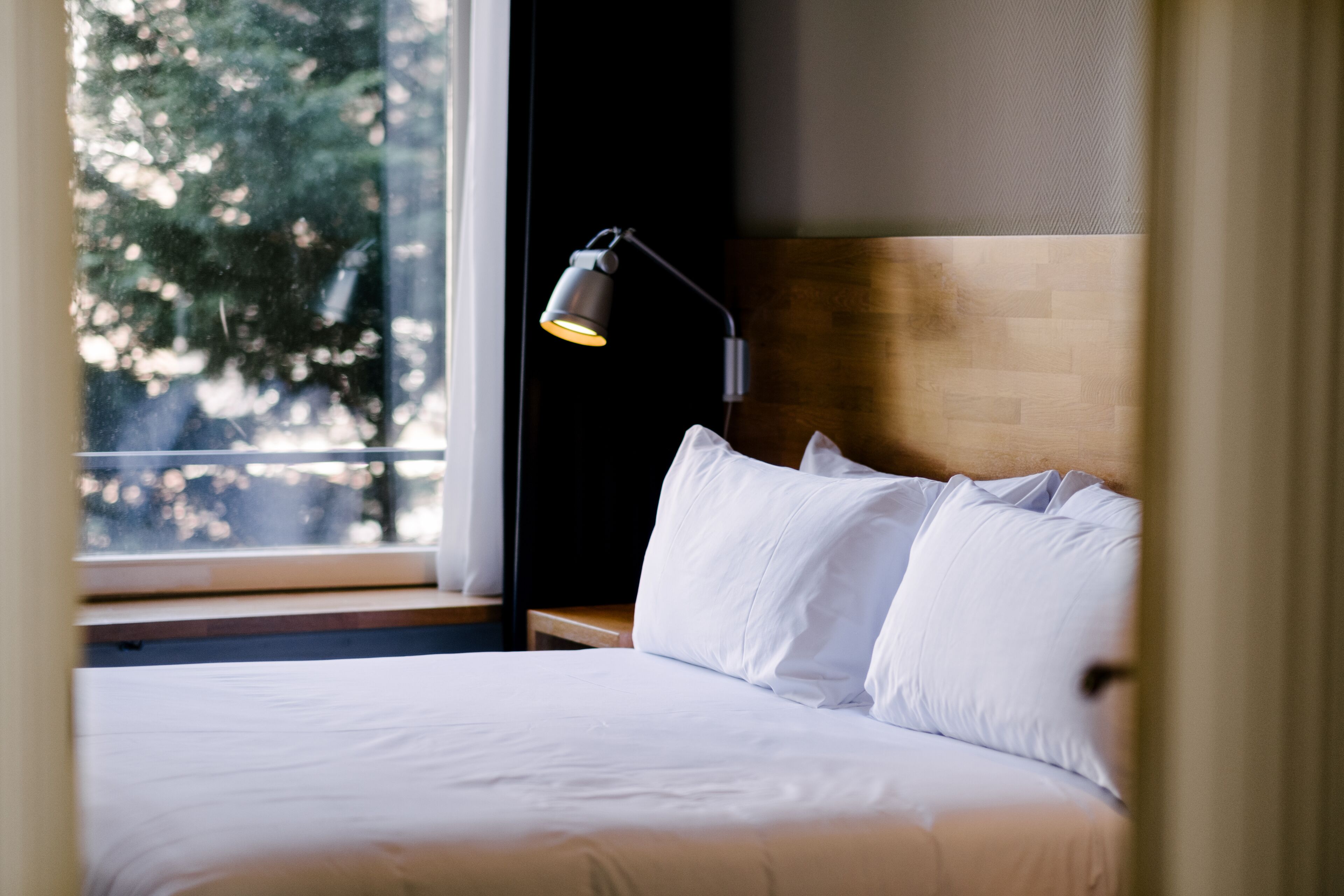 A neatly made bed with white linens and a single bedside lamp.