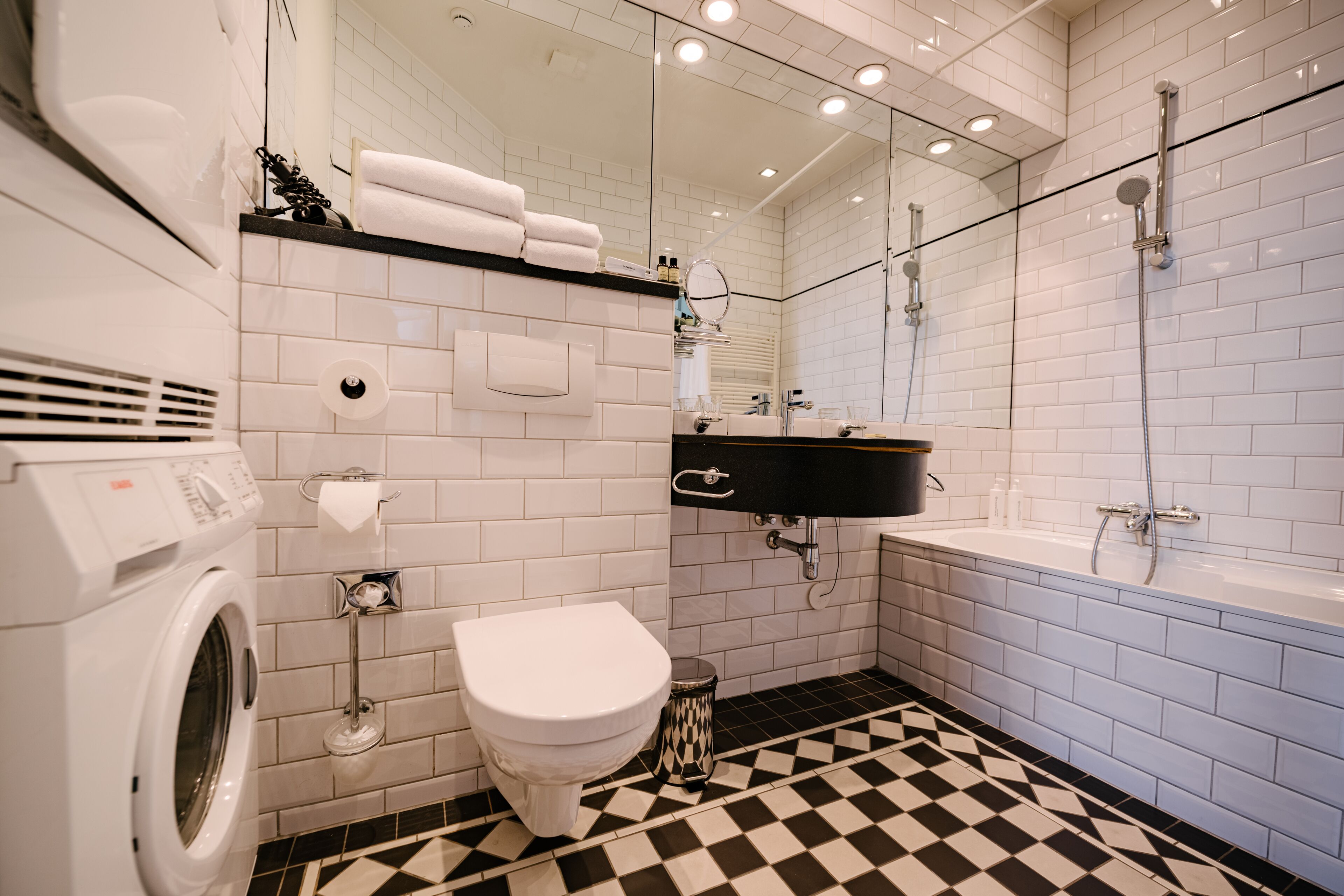 A bathroom with a black and white checkered floor, a white toilet, a washing machine, a sink, and a bathtub.