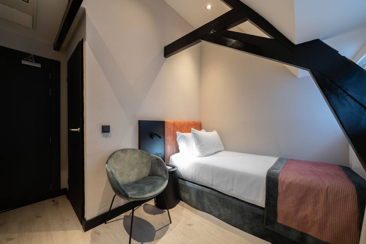 A small, modern bedroom with a single bed, a chair, and a desk.