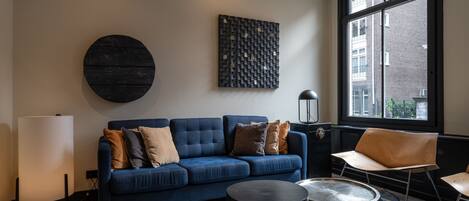 Una sala de estar moderna con un sofá azul, una mesa de centro redonda y un ventanal con vistas a edificios.