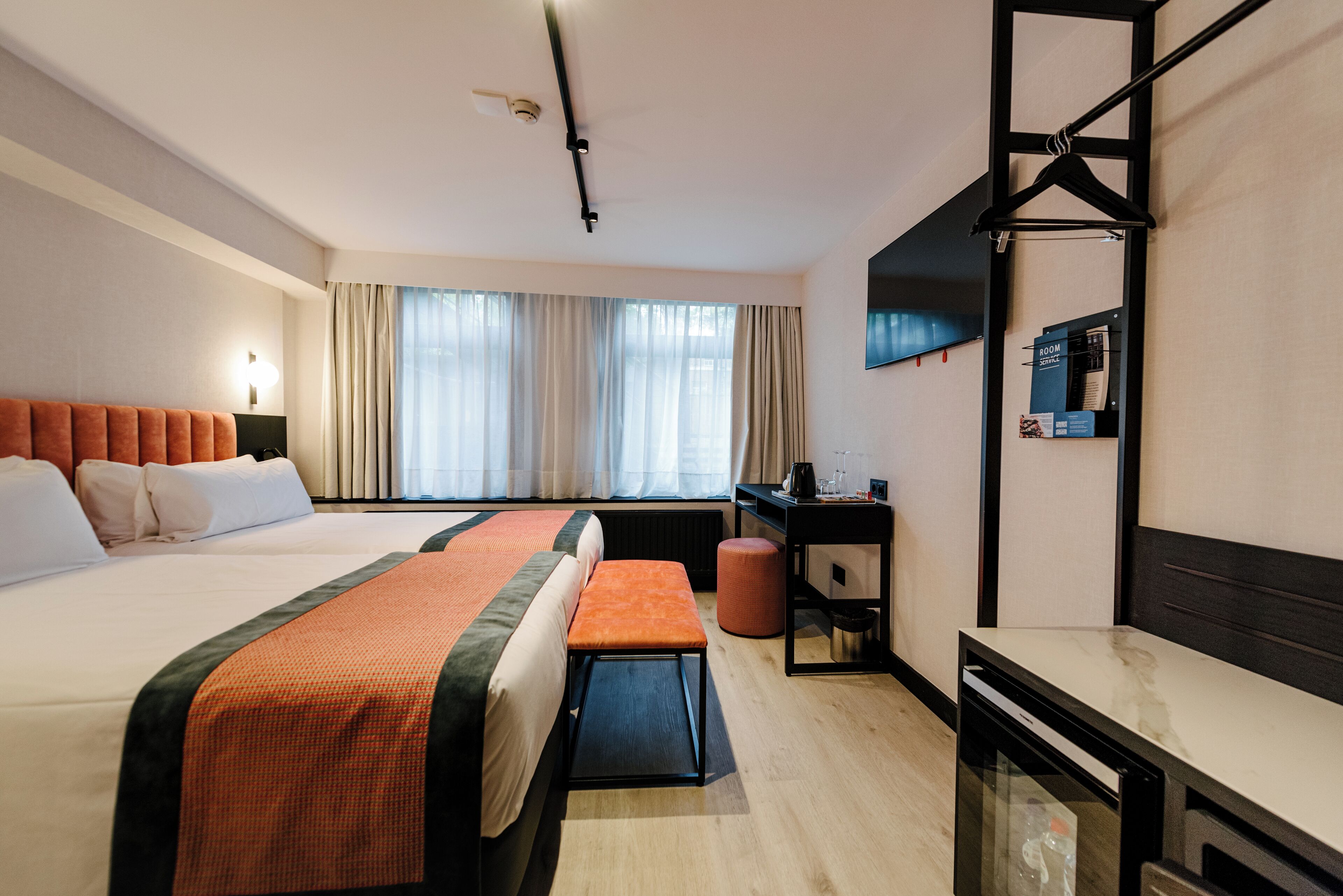 Une chambre d’hôtel avec deux lits, un bureau, une chaise, une petite table, un miroir et un téléviseur.