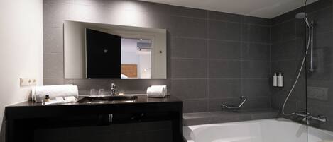 A modern bathroom with a large bathtub, a dark vanity with a mirror, and a shower area.
