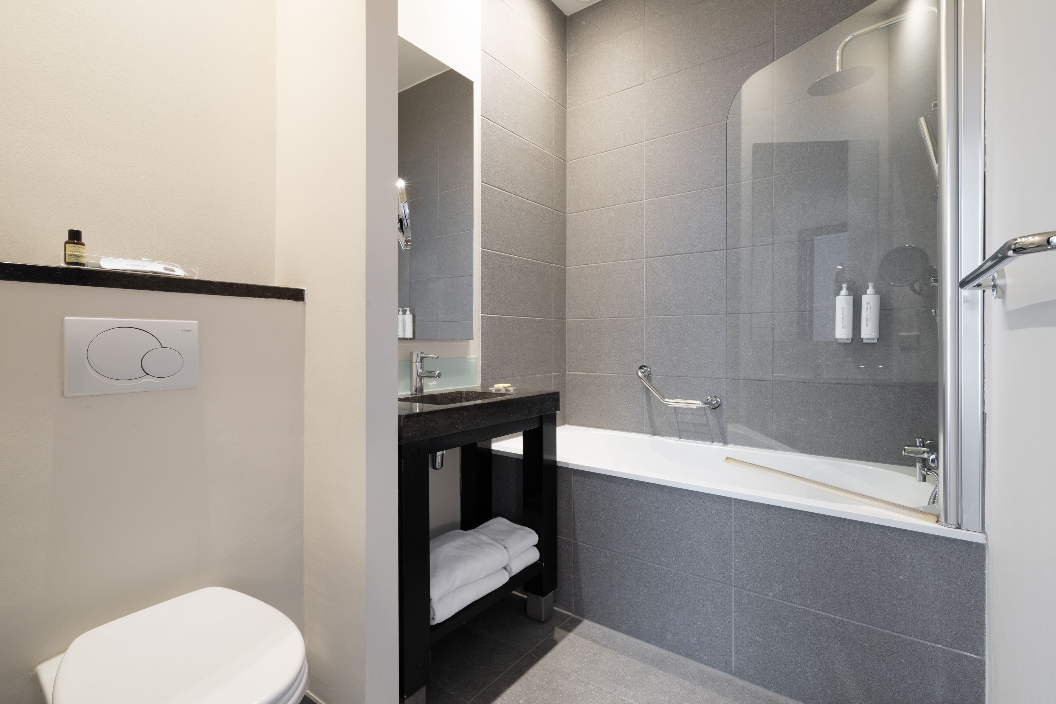 A modern bathroom with a toilet, a sink, a vanity, and a shower area.