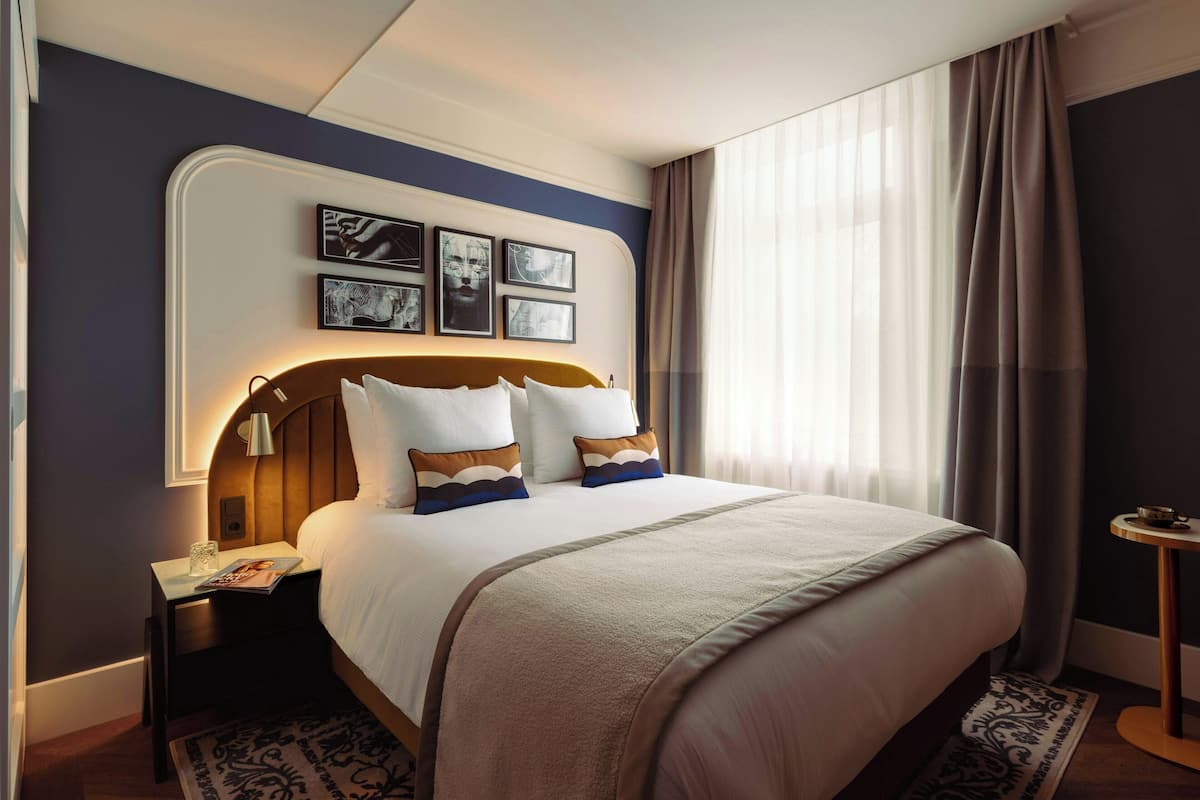 A neatly made bed with a headboard, a bedside table with a lamp, and framed pictures on the wall.