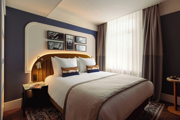 A neatly made bed with a headboard, a bedside table with a lamp, and framed pictures on the wall. - Leonardo Boutique Hotel The Lancaster Amsterdam (Amsterdam)