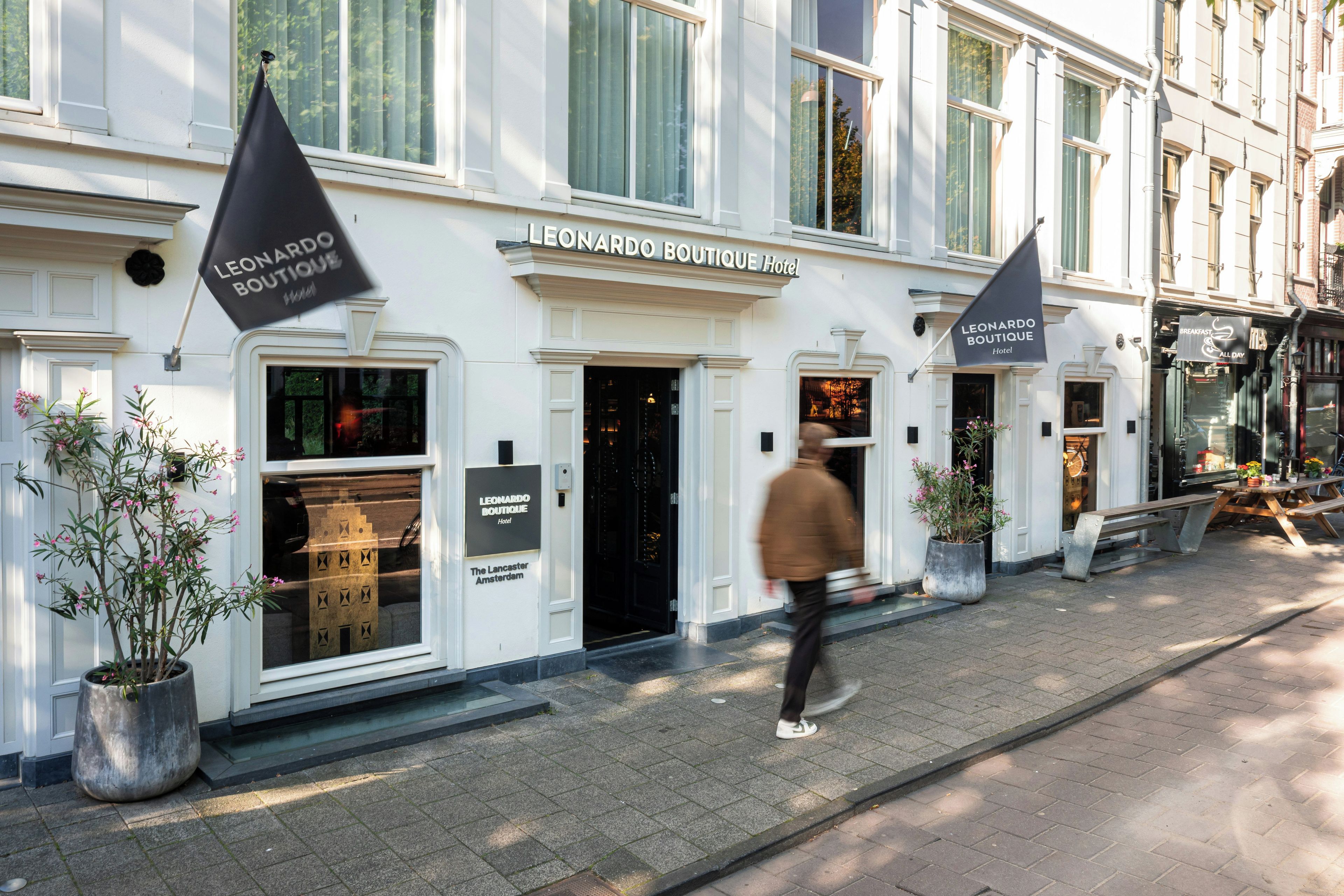 Een hotelgevel met een bord waarop 'Leonardo Boutique Hotel' staat. Er staan plantenbakken en een bank voor het hotel.