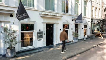 Een hotelgevel met een bord waarop 'Leonardo Boutique Hotel' staat. Er staan plantenbakken en een bank voor het hotel.