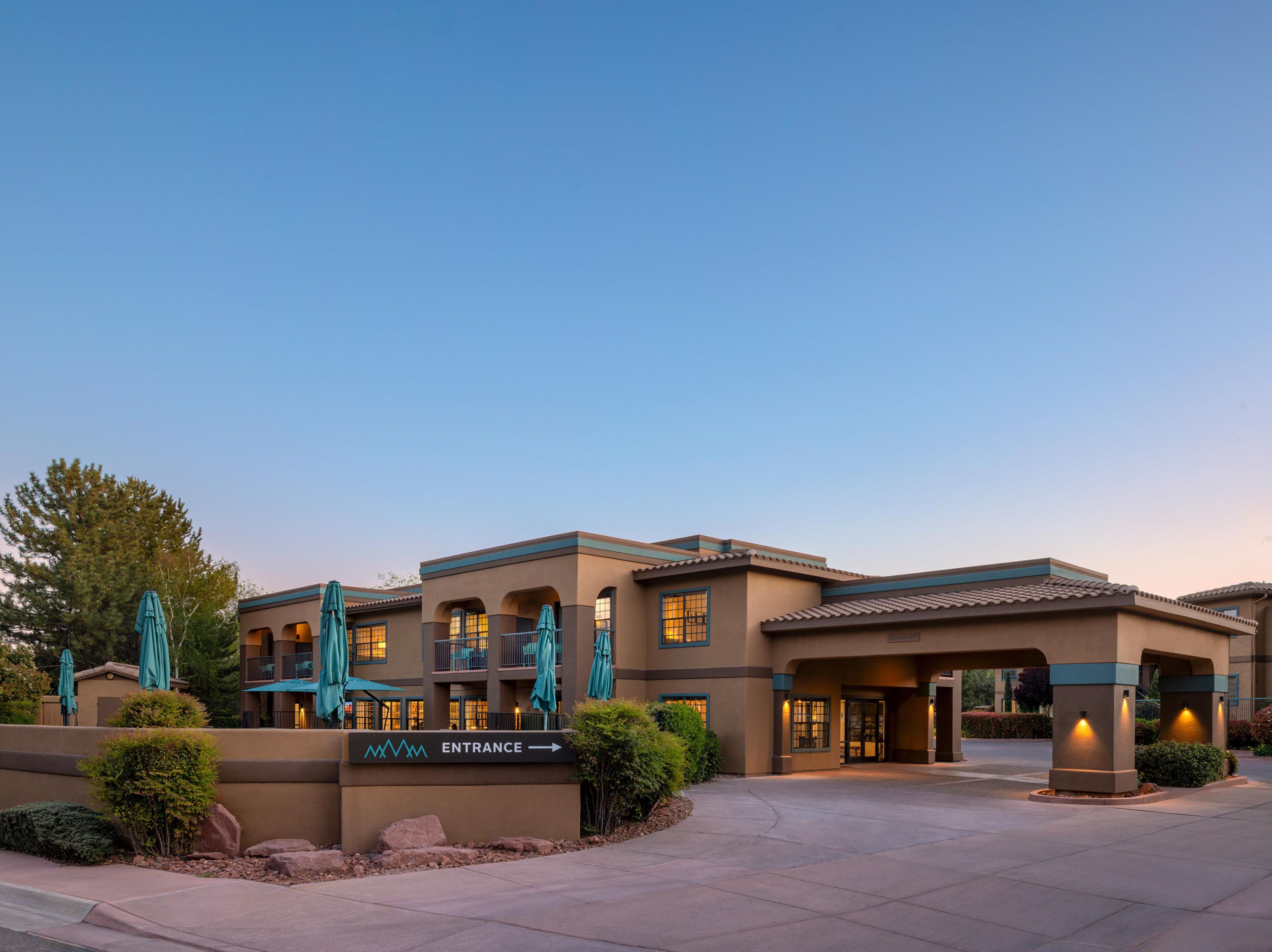 A hotel entrance with a sign, outdoor seating, and a clear sky.