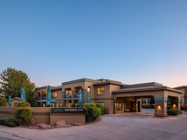 A hotel entrance with a sign, outdoor seating, and a clear sky.