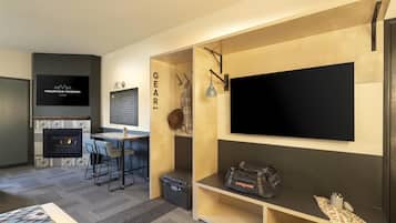 A modern living room with a fireplace, a TV mounted on the wall, a dining area with a table and chairs, and a shoe rack with boots and a bag.