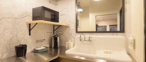 A modern bathroom with a large mirror, a white sink, and a microwave on a shelf.