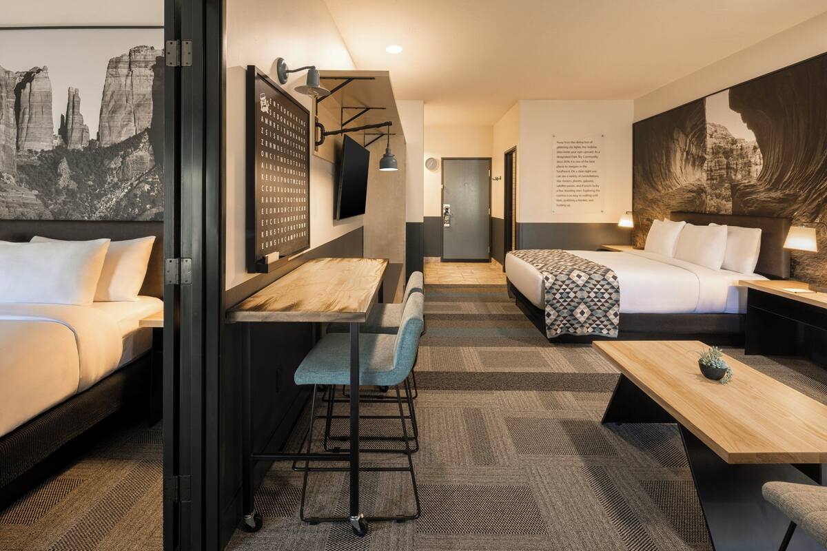 Une chambre d’hôtel comprenant un lit, un bureau, une chaise, une petite table et une grande œuvre d’art murale.